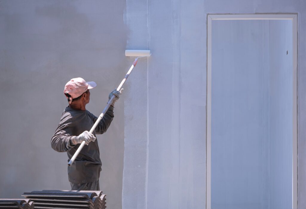 Construction worker painting primer white color on cement wall inside of house construction site