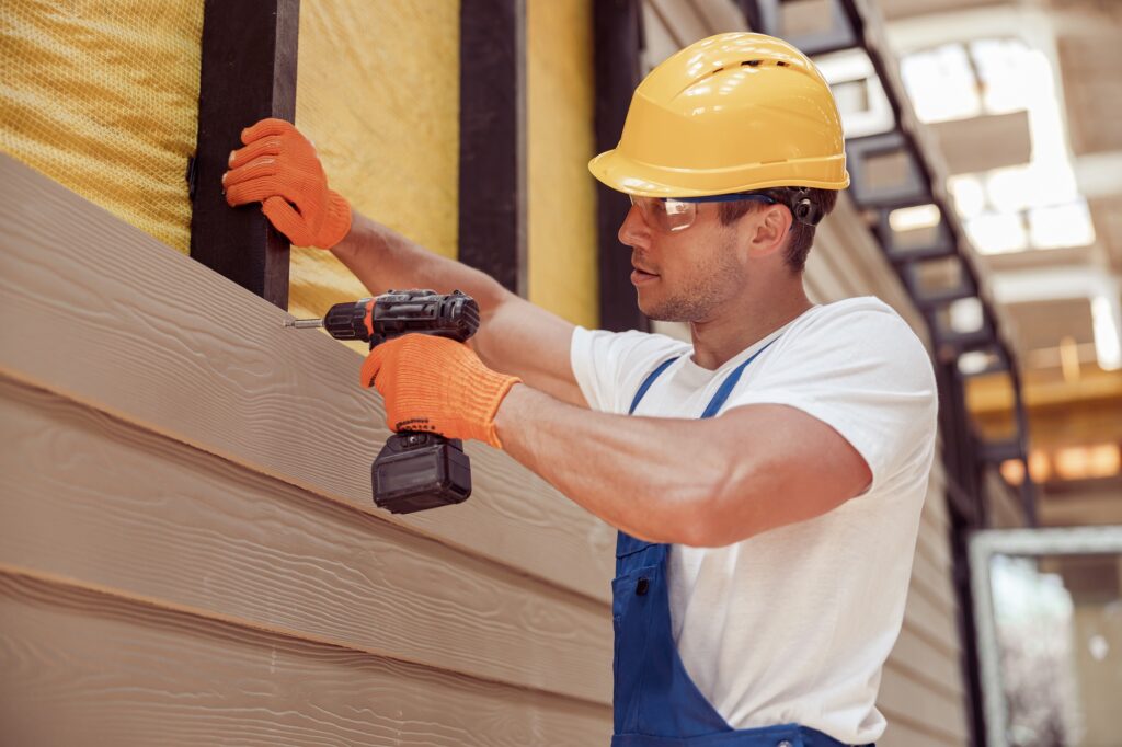 Male builder using power drill at construction site
